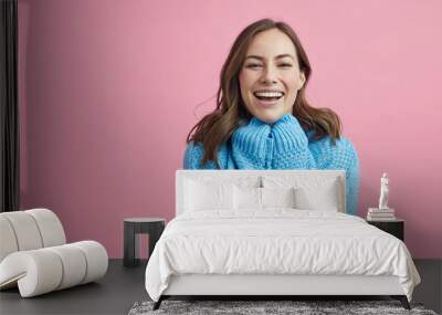 Portrait of happy and lovely young woman in a blue winter sweater on a pink background Wall mural