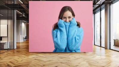 Portrait of happy and lovely young woman in a blue winter sweater on a pink background Wall mural