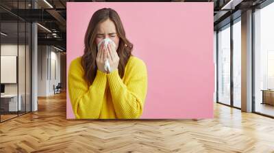 Pretty girl is Sneezing into a tissue because of her allergy or cold  Wall mural