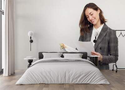 Smiling business woman with work in hands, standing isolated on white, looking happy about the papers she's reading and holding.  Wall mural