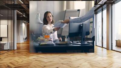 Young business woman receives more work from her coworker, while sitting at her desk. Wall mural