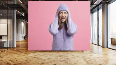 Young smiling woman looking happy and cute with purple sweater and matching hat, isolated on colorful pink background. Wall mural