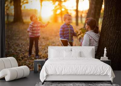 A working mother playing with kids during sunset in an autumn park Wall mural