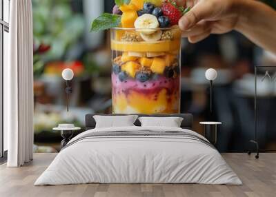 A vibrant and colorful fruit parfait is being assembled, showcasing layers of fresh fruits like mango, banana, and berries. presentation is visually appealing, perfect for refreshing treat Wall mural