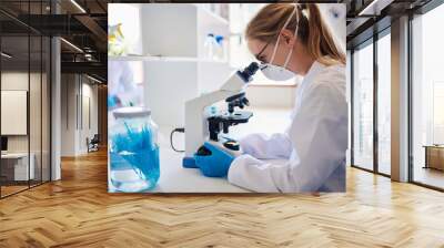 Female lab technician looking at samples in a microscope Wall mural