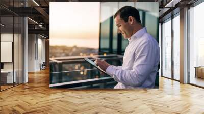 Smiling businessman standing on an office balcony using a tablet Wall mural