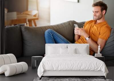 Smiling young man messsaging on his cellphone at home Wall mural