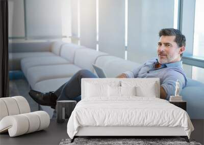 Stylish mature businessman smiling on couch with a digital tablet Wall mural