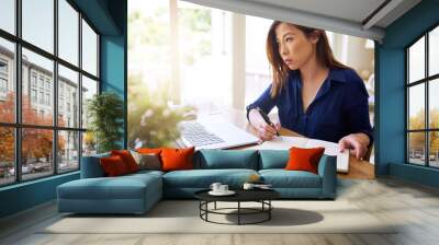 Young Asian businesswoman reading notes and working online from home Wall mural