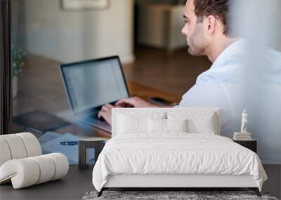 Young businessman sitting at a table at home using a laptop Wall mural