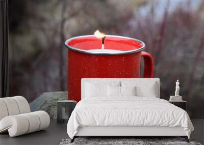 Red enamel cup candle sitting on wooden post outside.  Wall mural