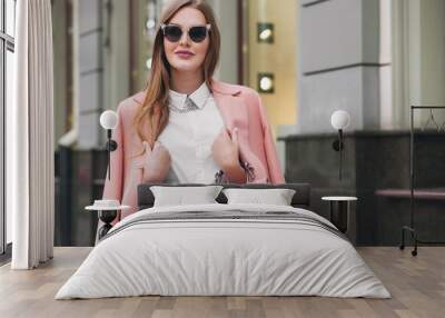 attractive stylish smiling rich woman walking city street in pink coat spring fashion trend holding purse, elegant style, wearing sunglasses Wall mural