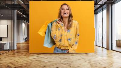 beautiful attractive smiling woman in yellow shirt and jeans holding shopping bags Wall mural