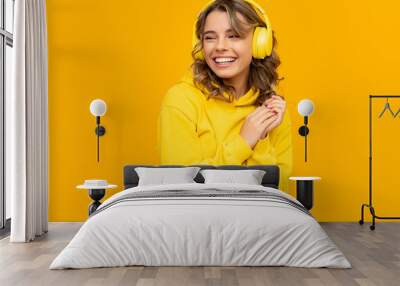 smiling attractive woman listening to music in headphones on yellow background Wall mural