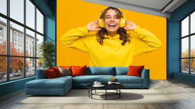 smiling attractive woman listening to music in headphones on yellow background Wall mural