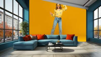 stylish happy smiling blond woman posing in jeans on yellow background Wall mural