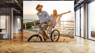 young attractive man and woman traveling on bicycles, romantic couple on summer vacation by the sea on sunset, boho hipster style outfit, friends having fun together Wall mural