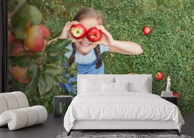 Apples for Children. Apples Eyes Kid. Apple Harvest. Little girl in blue apron put two apples to her eyes on grass background Wall mural