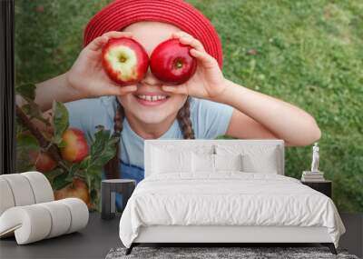 Apples for Children. Eco Organic Apple Harvest. Little girl in red hat holds two apples near the eyes on grass background.  Wall mural