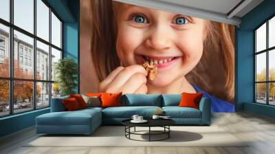 Little girl holding nuts near her mouth. Child smiles and eats walnut. Wall mural