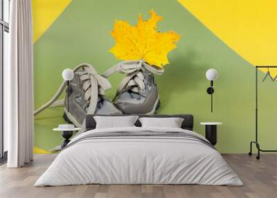 Autumn card: cute baby shoes with maple yellow leaf on yellow pastel background, space for text Wall mural