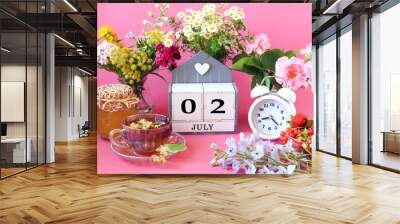 Calendar for July 2 : the name of the month of July in English, cubes with the numbers 0 and 2, a cup of tea, bouquets of flowers, an alarm clock, berries on a pink background Wall mural