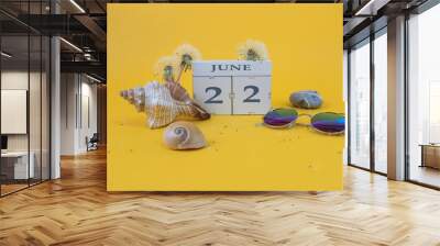 Calendar for June 22: cubes with the number 22, the name of the month of June in English, shells, sea stones, sunglasses, faded dandelions on a yellow background Wall mural