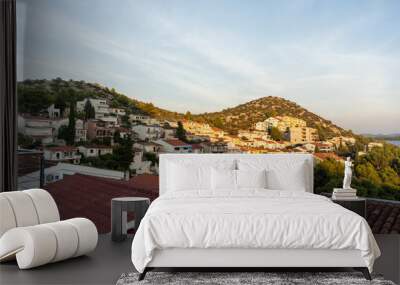 Scenic coastal village at sunset with red-roofed houses, green hills, and tranquil sea view. Wall mural