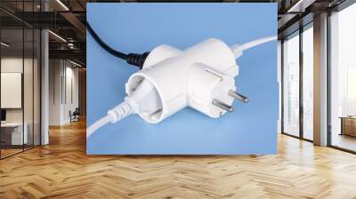 Tree plugs socketed into white electric splitter on a blue background. Splitter for simultaneous switching of three electrical appliances. Wall mural