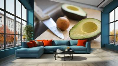 Avocado cut in half on a cutting board over a sink with knife in pit Wall mural