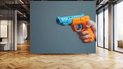 A child's hand clutches a colorful pistol against a plain gray background. Wall mural