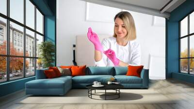 A female doctor puts on pink gloves before a medical examination. Hygiene and health Wall mural