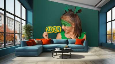 A happy attractive laughing girl with mask holds the numbers of the 2024 new year. Headdress in the shape of dragon wings Wall mural