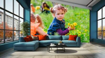 little curly girl sitting on the grass. a child holding a dandelion. girl with two tails on head smi Wall mural