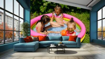 Three girls are having fun in a small inflatable swimming pool in the garden on a hot sunny day. Children play with a watering can in the water. Outdoor recreation Wall mural