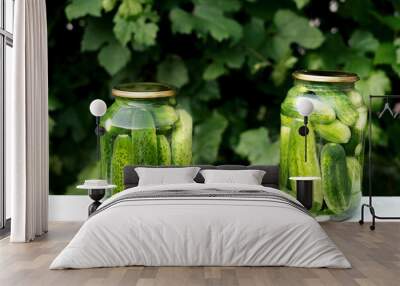 Two cans of canned cucumbers and garlic stand on a white table against the background of green grape leaves Wall mural