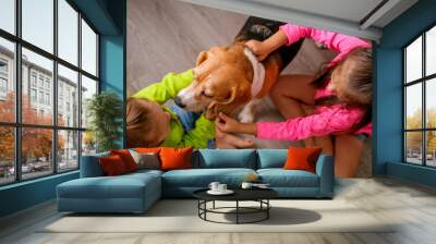 Two little sister girls play with a dog, caressing her sitting on the floor in the room. Development of allergy to dog hair in children Wall mural