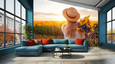 Back view of woman enjoying view in blooming sunflower field at sunset with bouquet of flowers. Peace and freedom Wall mural