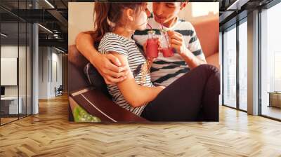 Couple in love drinking smoothie chilling on sofa in living room. Man and woman hugging enjoying drinks Wall mural