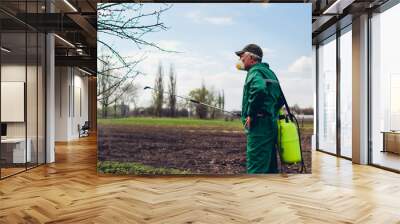 Farmer spraying tree with manual pesticide sprayer against insects in spring garden. Agriculture and gardening Wall mural