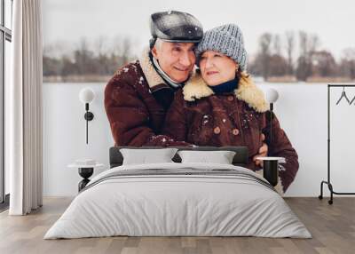 Portrait of senior family couple walking outdoors during snowy winter weather. Mature people hugging Wall mural