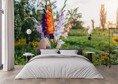 Woman gardener holding bunch of fresh gladiolus in summer garden. Farmer picked bouquet of flowers Wall mural