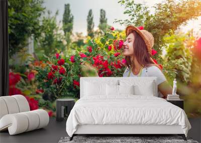 Young woman gathering flowers in garden. Girl smelling and admiring roses. Gardening concept Wall mural