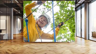 Boy in special equipment, protective helmet and gloves, laughs having fun in activity with ladder rope park. Bright casual wear. outdoors, green trees around there. Wall mural