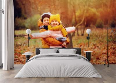 autumn portrait of happy kids playing outdoor in park. Smiling brother and sister walking in sunny day, wearing warm knitted hats and scarfs Wall mural