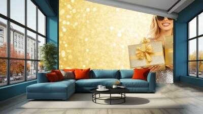 Smiling woman holding gold presents in a sparkling golden background, perfect for holiday celebrations. Wall mural