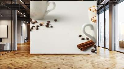 Two mugs of hot coffee topped with whipped cream and nuts, surrounded by spices and coffee beans on a white background. Cozy winter drink concept. Wall mural