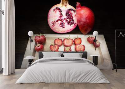 A colorful and heart composition for two excellent fruits: strawberries and pomegranates, positioned on an old table and illuminated using light painting technique. Wall mural