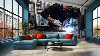 Performing a weld: the man in the welding mask is positioned with the welding machine on the welding point. When he activates it, a blue glow with smoke and orange sparks illuminates the scene. Wall mural