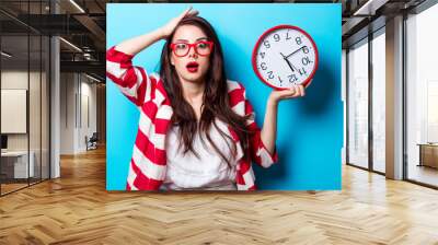 beautiful surprised young woman with clock standing in front of wonderful blue background Wall mural